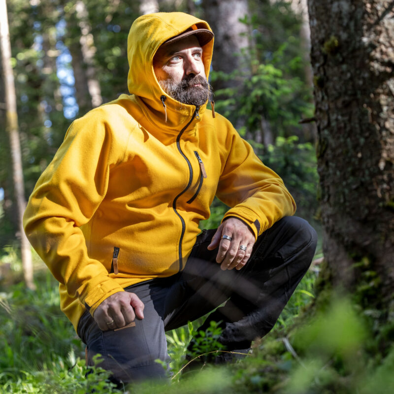 Mann mit gelber Lodenjacke im Wald kniend